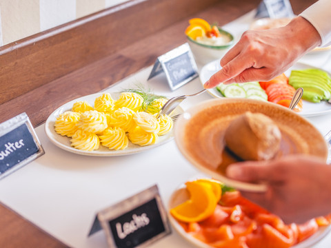 Café Die alte Schule Hände eines Menschen servieren sich frische Brötchen von einem reichhaltigen Frühstücksbuffet.