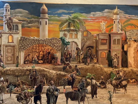 Golfclub Orientalische Krippe Ein kunstvoll detailliertes Krippendorf bei Sonnenuntergang, mit Figuren beim Alltag in einem orientalischen Setting.