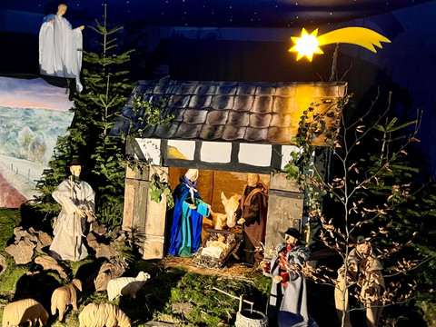 Krippe St. Martinus Krippenszene mit leuchtendem Weihnachtsstern, Maria, Joseph, Hirten und Tieren in einer Scheune.