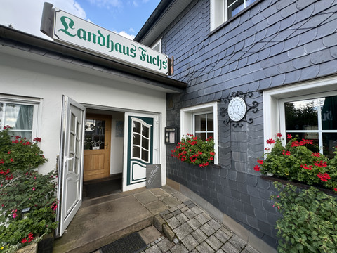 Landhaus Fuchs - Ansicht Eingangsbereich Landhaus Fuchs in Kürten, charmantes Gasthaus mit grauer Schieferfassade und blühenden Geranien.