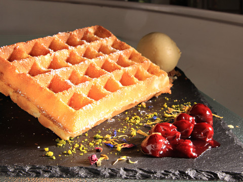 Waffel.jpg Belgische Waffel auf schwarzem Stein serviert, daneben Kugel Pistazieneis und eingemachte Kirschen.