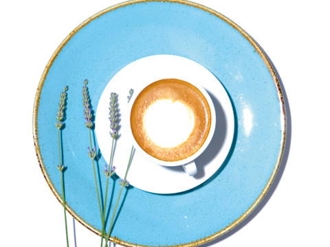 Latte Macchiato.jpg Tasse Cappuccino auf weißem Teller, umrahmt von frischen Lavendelstängeln auf hellblauem großen Teller.