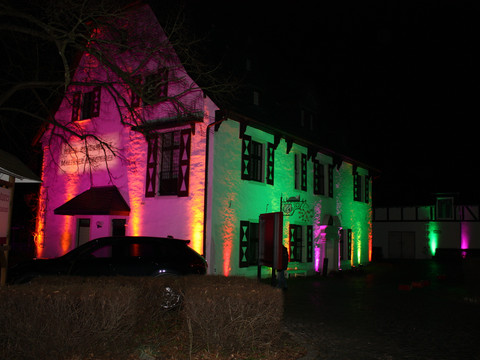 Malteser Komturei-4 Historisches Gebäude in Bergisch Gladbach, nachts bunt beleuchtet, mit dunklen Fenstern und Umgebung.