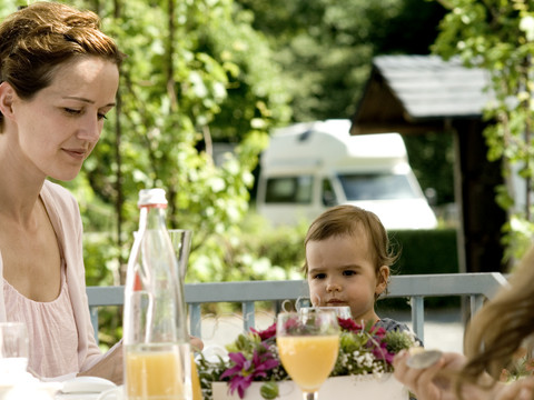 Gäste Eine Frau und ein Kind genießen draußen ein Frühstück an einem Tisch mit Blumen und Orangensaft.