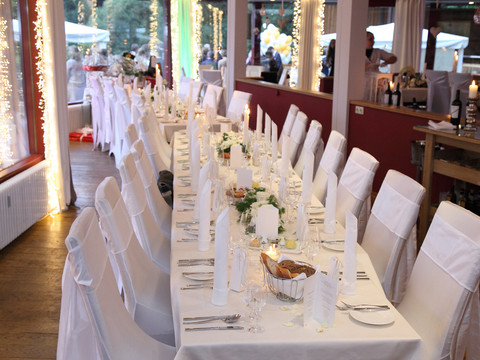 Festsaal -2 Ein festlich gedeckter, langer Esstisch mit weißen Stuhlhussen in einem eleganten, beleuchteten Raum.