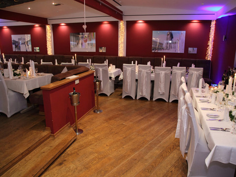 Festsaal -1 Elegantes Restaurant in Bergisch Gladbach mit weiß gedeckten Tischen, roten Wänden und Kerzenlicht.
