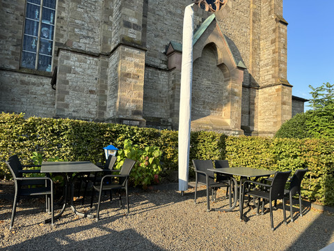 Dürscheider Hof - Ansicht Biergarten <p>Gepflegter Außenbereich mit vier schwarzen Tischen und Stühlen vor einer historischen Steinmauer.</p>