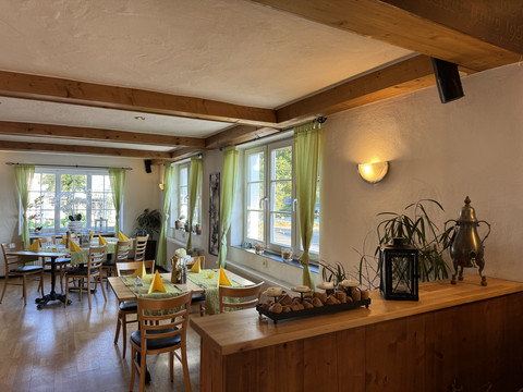 Dürscheider Hof - Innenansicht Gemütliches Café mit Holzmöbeln, Pflanzen und Tageslicht durch große Fenster.