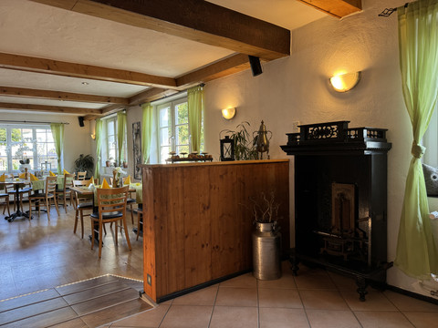 Dürscheider Hof - Innenansicht Holzvertäfelte Gaststube mit Kamin, gedeckten Tischen und grünen Vorhängen in einem gemütlichen Restaurant.