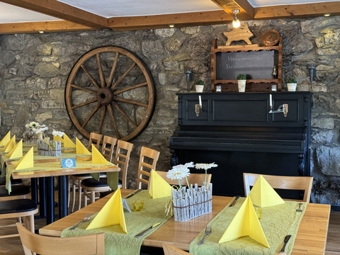 Dürscheider Hof - Innenansicht Gemütliches Restaurant mit Steinmauer, dekoriert mit einem Wagenrad und einem antiken schwarzen Klavier.