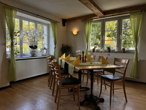 Dürscheider Hof - Innenansicht Gemütlicher Essbereich mit Holztisch und Stühlen, dekoriert mit gelben Servietten und grünen Vorhängen.