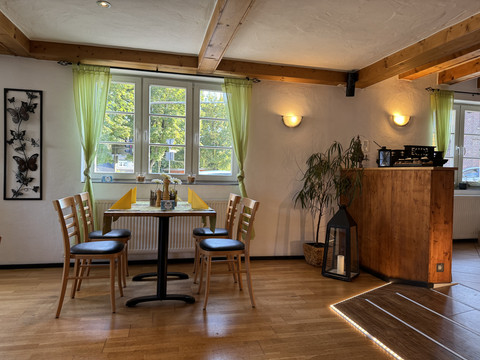 Dürscheider Hof - Innenansicht Gemütliches Café mit Holzmöbeln, gedecktem Tisch und großen Fenstern mit grünem Vorhang.