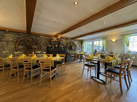 Dürscheider Hof - Innenansicht  Gemütliches Restaurant mit Holzmöbeln, gelben Servietten, Steinwänden und großen Wagenrädern an der Wand.