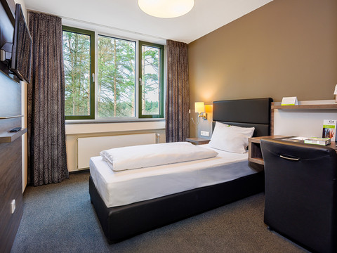 Einzelzimmer Ein gemütliches Einzelzimmer mit modern eleganten Möbeln, großen Fenstern und einem bequemen Bett.