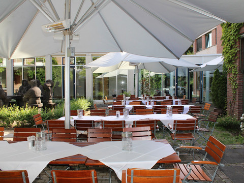Terrasse Gemütlicher Außenbereich eines Restaurants mit Holzmöbeln und weißen Sonnenschirmen auf Terrassenpflaster.