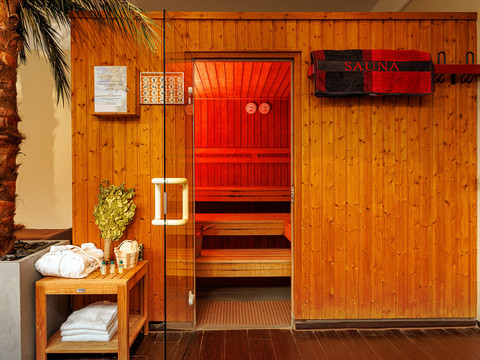 Sauna Holzverkleidete Sauna, mit offener Glastür. Daneben Handtücher und Birkenzweige auf einem Tisch.