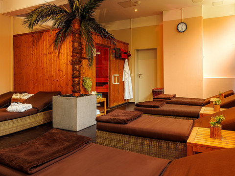 Sauna Entspannungsraum mit Liegen, Handtüchern, Pflanzen und einer Palme, ideal für Ruhe und Erholung.