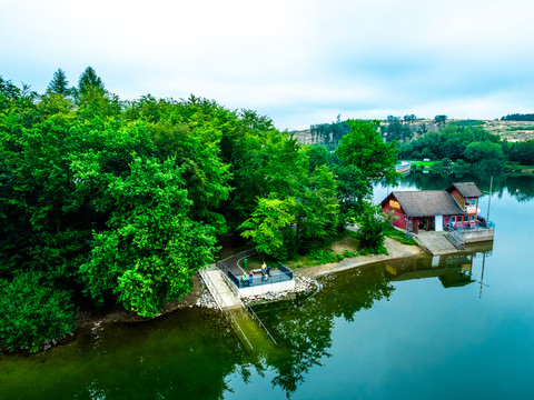Brucher Talsperre aus der Luft Ein See mit angrenzendem Wald und einem Steg, der zu einem kleinen, hölzernen Gebäude führt.