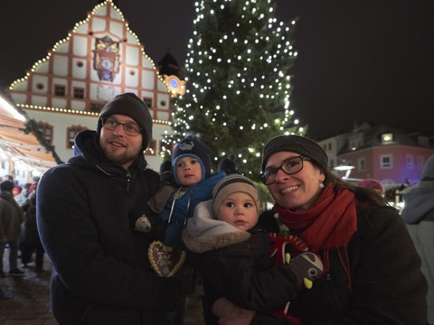Familie auf dem Plauener Weihnachtsmarkt_ArchivTVV-TinoPeisker.jpg Eltern mit zwei Kindern auf einem festlich erleuchteten Weihnachtsmarkt bei Nacht.
