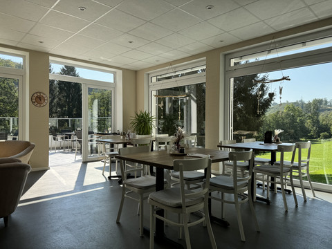 Kaffeerösterei Pagnia - Innenansicht Moderne, lichtdurchflutete Caféecke mit weißen Möbeln und großem Panoramablick ins Grüne.