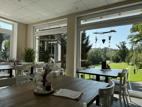 Kaffeerösterei Pagnia - Innenansicht Ein helles Café mit großen Fenstern, Blick ins Grüne, weißen Stühlen und natürlichen Dekorationen.