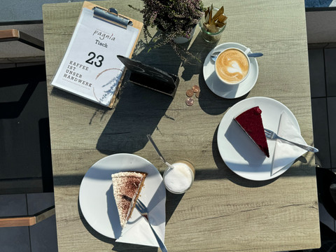 Kaffeerösterei Pagnia - Ansicht Kaffee & Kuchen Kaffee und Kuchen auf einem Holztisch, mit Cappuccino, Tiramisu und Rote-Bete-Kuchen serviert.