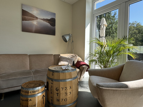 Kaffeerösterei Pagnia - Innenansicht Gemütliche Lounge mit Sofa und Sessel, weinbarell als Tisch, helle Fensterfront mit Blick ins Grüne.