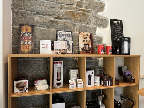 Kaffeerösterei Pagnia - Ansicht Austellungsregal Regale mit Kaffeespezialitäten, Geschirr und Kaffeemaschinen vor einer Steinwand.