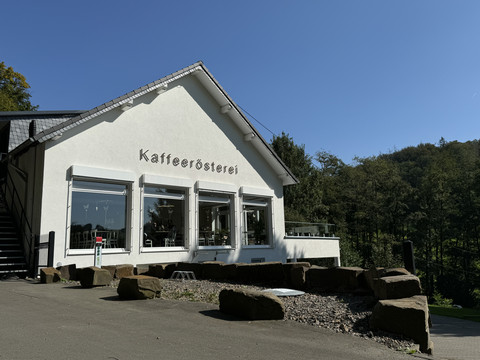Kaffeerösterei Pagnia - Außenansicht Ein weißes Gebäude mit der Aufschrift "Kaffeerösterei", umgeben von Bäumen und blauen Himmel.