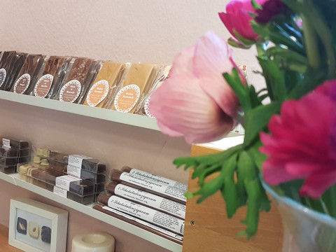 CL_laden3.jpg In einem gemütlichen Raum stehen auf Regalen handgemachte Schokolade und Pralinen, umgeben von frischen Blumen.