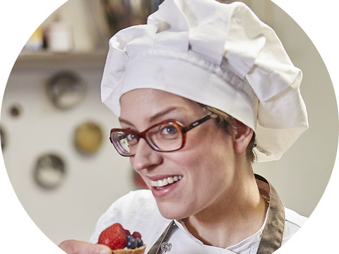 Eva.jpg Köchin mit Brille und weißer Mütze genießt eine Fruchttarte in einer gemütlichen Küche.