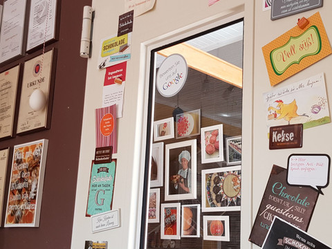 laden2.jpg Ein geschmückter Schokoladenladen mit Urkunden, Bildern und dekorativen Schildern an der Wand.