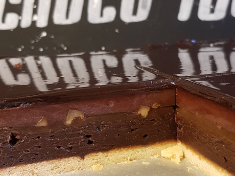 schokoschock.jpg Nahaufnahme einer angeschnittenen Schokoladentorte mit glänzender Glasur und nussiger Füllung.