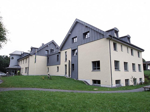 Jugendherberge Wiehl Barrierefreies, modernes Gebäude in Wiehl mit gelber Fassade und grauen Akzenten im Grünen.