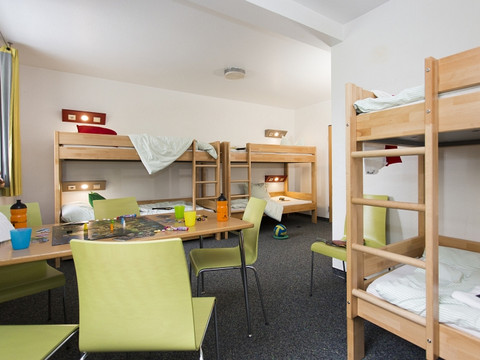 Jugendherberge Wiehl Ein gemütlicher Gemeinschaftsraum mit Stockbetten, Tisch, grünen Stühlen und verstreuten Spielsachen.