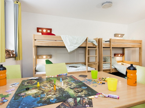 Jugendherberge Wiehl Ein heller Raum mit Etagenbetten, Spielen auf einem Tisch sowie orange und grüne Trinkflaschen.