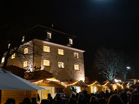 Bielsteiner Weihnachtsmarkt rund um die Burg Nächtlicher Weihnachtsmarkt mit festlich beleuchteten Buden und einem erleuchteten Gebäude im Hintergrund.