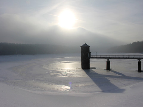 Die Talsperre im Winter mit vereistem Wasser und aufziehendem Hochnebel