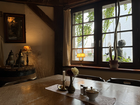 Pfannkuchenhaus Nümbrecht - Innenansicht Gemütlicher Innenraum eines Cafés mit Holztisch, Kerzen, nostalgischer Deko und Blick auf eine Skulptur.