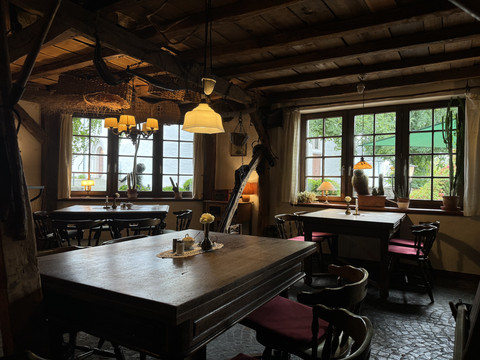 Pfannkuchenhaus Nümbrecht - Innenansicht Eine gemütliche Stube mit Holzmöbeln, dezenten Lampen und Fenstern mit Blick auf grüne Natur.