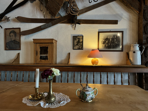 Pfannkuchenhaus Nümbrecht - Innenansicht Rustikaler Raum mit antiken Ski, Fotos und Lampe an der Wand; Tisch mit Kerzenleuchter und Teekanne.