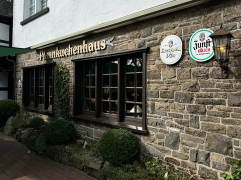 Pfannkuchenhaus Nümbrecht - Außenansicht Fachwerkhausfassade mit Holzfenstern, "Pfannkuchenhaus"-Schriftzug, Schilder zu Bieren an Steinwand.