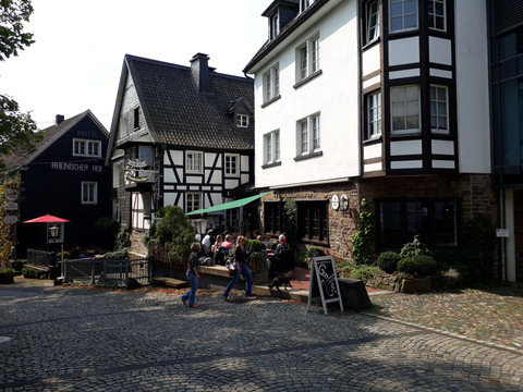 Pfannkuchenhaus Nümbrecht - Außenansicht Fachwerkhäuser im historischen Ortskern von Nümbrecht, Deutschland, mit Menschen auf einem Cafévorplatz.