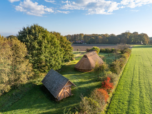 Luftaufnahme zweier traditioneller Häuser in grüner Landschaft, umgeben von Bäumen und Feldern.