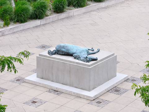 05_KSC_Collateral Sculptures_MutterGenth_Pferd.jpg Skulptur eines liegenden Pferdes auf einem Podest, umgeben von steinernem Pflaster und Grünflächen.Sculpture of a reclining horse on a pedestal, surrounded by stone paving and green areas.Socha ležícího koně na podstavci, obklopená kamennou dlažbou a zelení.Rzeźba leżącego konia na cokole, otoczona kamiennym brukiem i terenami zielonymi.Sculptuur van een liggend paard op een sokkel, omgeven door stenen bestrating en groene zones.Scultura di un cavallo sdraiato su un piedistallo, circondato da pavimentazione in pietra e aree verdi.