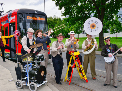 A jazz band plays in front of a red streetcar on a sidewalk.