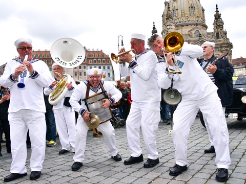 Dixielandfestival-Dixieland-Parade-3-©-Foto-Hendrik-Meyer.jpg Musicians in sailor suits play live on a cobbled street, surrounded by onlookers.