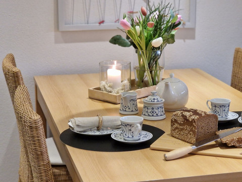 Esszimmer Ein gedeckter Holztisch mit Kerzen, Blumen, Keramikgeschirr und angeschnittenem Brot.