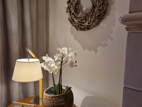 Kranz Runder Holztisch mit Lampe, Orchidee im Korb und Bildrahmen, daneben rustikales Ast-Dekor an der Wand.