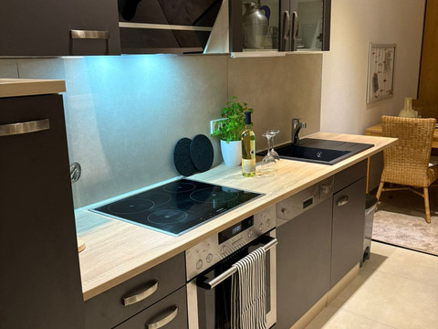 Küche_01 Moderne Küche mit dunklen Schränken, hellem Holz, Geschirrspüler und Kochfeld, gemütlich gestaltet.